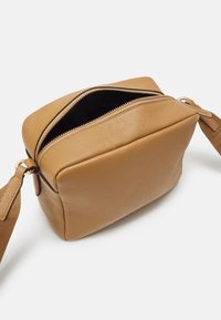 Hnědá kožená kabelka obdélníkového tvaru, s horním zipem a jedním nastavovacím popruhem. Hladký povrch bez viditelných vzorů.