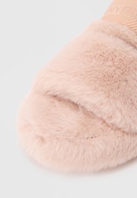 Fluffy lyserøde hjemmesko med blød tekstur og brede stropper. Materialet ser overdådigt ud og skaber et hyggeligt design til indendørs brug.