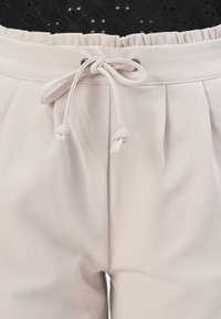 Light beige pants with an elastic waistband and drawstring. Smooth texture, featuring pleats at the front and subtle sheen.