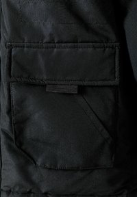 Tissu noir matelassé avec une poche avant dotée d'un rabat et d'un contour surpiqué. La texture semble lisse avec un léger éclat.