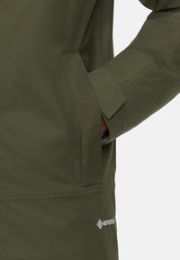 Grøn Gore-Tex jakke med en skjult lomme, pæne syninger og en glat overflade. Ergonomisk pasform med knappede manchetdetaljer.