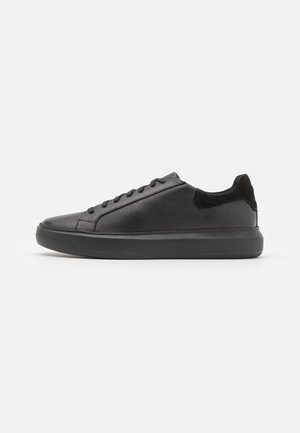 Sneakers in pelle nera con una texture liscia, punta rotonda e accenti in suede nero a contrasto sul tallone e sulla linguetta. Suola in gomma.