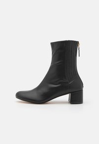 Bota negra de cuero hasta el tobillo con un diseño elegante, puntera redondeada y un tacón bajo; cuenta con costuras verticales y un cierre lateral con cremallera.
