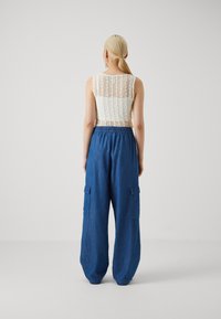 Hvit blonde toppen med rygdesign, kombinert med løse, blåe cargobukser med sidelommer og elastisk midjebånd.