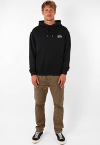 Hoodie noir avec poche avant, cordons de serrage et logo sur la poitrine gauche. Associé à un pantalon cargo khaki et des baskets noires.