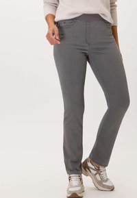 Pantalons de sport gris avec une taille mi-haute, design classique à cinq poches et coupe slim, associés à des baskets de sport de couleur claire.