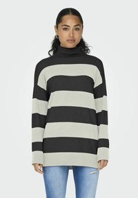 Gestreepte coltrui in donkergrijs en lichtgrijs, met een losse pasvorm en ribgebreide manchetten, gecombineerd met blauwe jeans. Zacht gebreid materiaal.