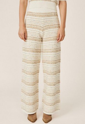 Persona con pantalones de punto de cintura alta y pierna ancha con rayas horizontales beige y blancas y botas marrones con punta estrecha.