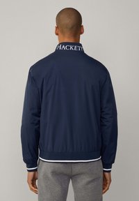 Marine bomberjakke med høj krave, hvid "HACKETT" logo på kraven, elastiske ærmer og talje. Glat, let materiale.