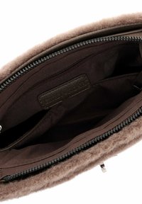 Ruskea villakäsilaukku, jossa on vetoketjullinen yläosa, sileällä sisävuorella ja pieni vetoketjupussi sisällä. Ulkopinta on teksturoitu ja pehmeä.