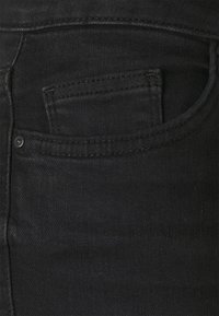 Vaqueros de denim negro con una textura suave, que cuentan con un bolsillo trasero, costuras sutiles y un detalle de botón metálico.