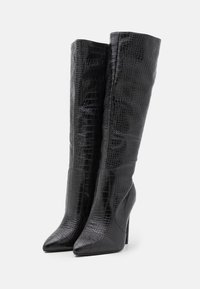 Bottes noires jusqu'au genou avec une texture crocodile, un bout pointu, un talon haut et des accents en cuir lisse le long des côtés.