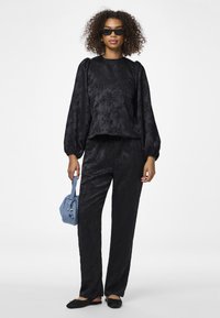 Completo nero texturizzato composto da una maglietta con maniche a sbuffo e pantaloni dritti. Gli accessori includono una piccola borsa blu e scarpe nere flat.