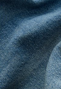 Prim-plan al țesăturii de denim albastru, evidențiind textura detaliată a țesăturii și pliurile subtile din material.