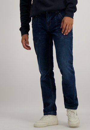 Donkerblauwe denim jeans met een recht model, voorzien van vijf zakken en subtiele stiksels, gedragen met witte sneakers.