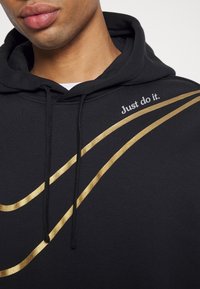 Svart hoodie med guld detaljer och texten "Just do it." i vitt. Tillverkad av ett mjukt tyg med en dragsko i huvan.