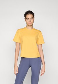 T-shirt jaune à manches courtes en tissu doux, avec un col rond et une coupe courte, associé à un legging bleu ajusté.