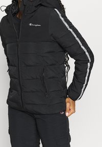 Black padded jacket with a hood, featuring a front zipper, side pockets, and gray striped accents on the sleeves. Made of smooth material.