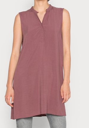Mouwloze mauve tuniek met een korte knoopsluiting, gedragen over grijze broek bij een persoon tegen een lichte achtergrond.