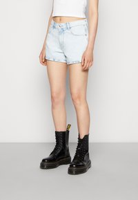 Světle modré džíny s vysokým pasem a potrhaným lemem, kombinované s černými platformovými botami na šněrování s žlutými akcenty.