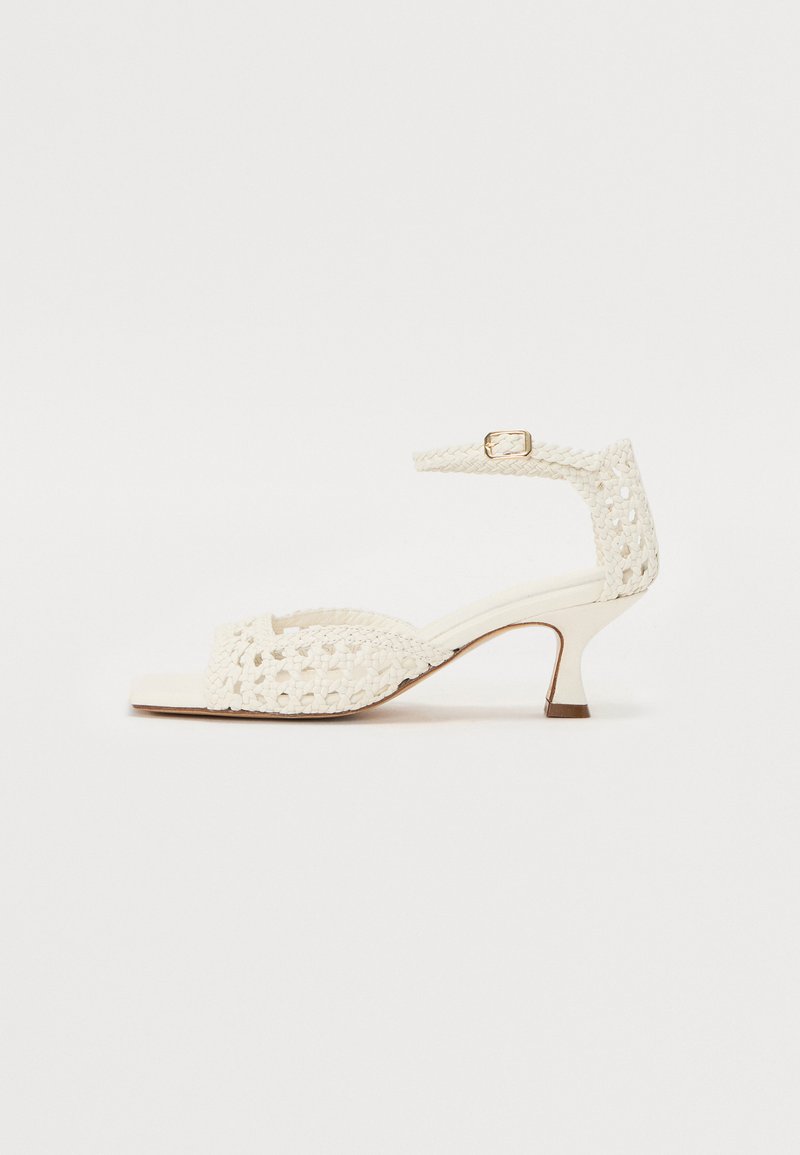 Witte geweven sandaal met een lage hak, voorzien van een decoratieve enkelband en open teenontwerp. Soepele textuur met subtiele details.