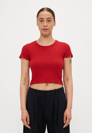 Rød ribbet crop-top med korte ærmer, med rund hals og bølget kant. Kombinert med høytlivede svarte plisserte bukser.