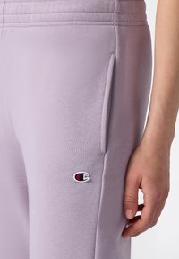 Pantalones deportivos de color lavanda en tejido suave, con bolsillos laterales y logo bordado, que cuentan con costuras texturizadas a lo largo de la cintura.