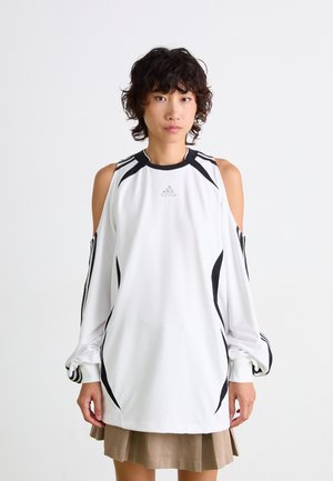 Chemise blanche à manches longues avec découpes épaules dénudées, accents de rayures noires et texture subtile. Logo Adidas centré sur la poitrine.