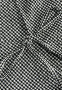 Tissu vichy noir et blanc avec un gros plan sur un nœud formé par deux bandes de tissu qui se croisent.