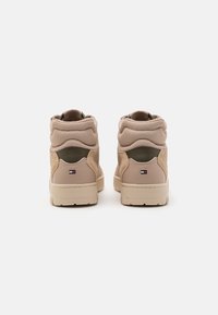 Beige high-top sneakers met gewatteerde kraag, textuurstofdetails, dikke rubberen zolen en kleine rechthoekige logo's op de hielen op een witte achtergrond.