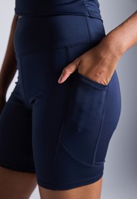 Shorts bleu marine en tissu extensible, dotés d'une poche latérale et de coutures apparentes pour plus de durabilité et de design.