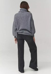 Szary sweter z dzianiny z wysokim kołnierzem i luźnymi rękawami, w połączeniu z czarnymi spodniami o szerokich nogawkach. Tekstura wydaje się miękka i przytulna.