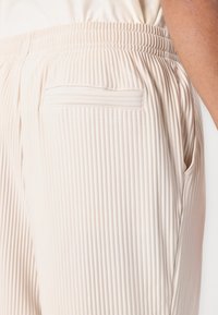 Lichtbeige geribde joggingsbroek met een elastische tailleband, voorzien van een zijzak en een achterzak voor opslag.
