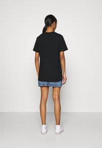 Camiseta de algodón negra con mangas cortas, mostrada desde la parte posterior, combinada con una falda de mezclilla. Zapatillas altas blancas completan el look.