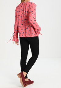 Rosa långärmad blus med ett geometriskt mönster, matchad med svarta tighta byxor och burgundy klackskor. Ribbonsnoddar som accent på ärmarna.