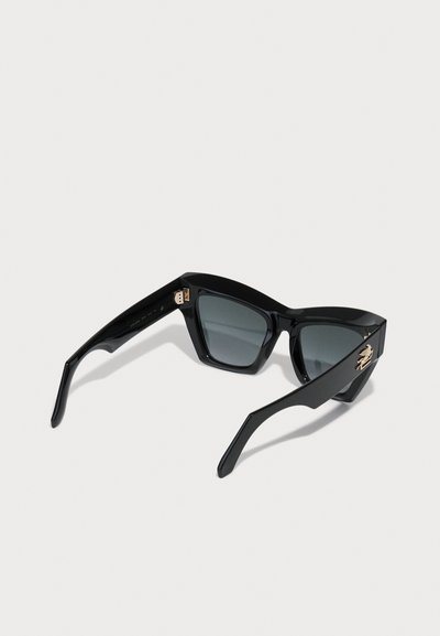 Črne sončne očala s obliko mačjih oči, temnimi lečami, sijajnim plastičnim okvirjem in zlatim poudarkom na strani. Teksturiran dizajn tempelj.