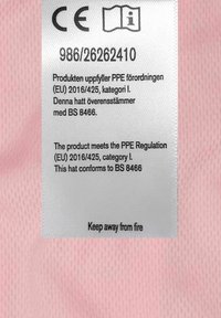 Valkoinen kangasmerkintä, jossa on teksti useilla eri kielillä, vaaleanpunaisella verkkotaustalla ja turvallisuusvaroituksia, mukaan lukien "Pidä kaukana tulesta."