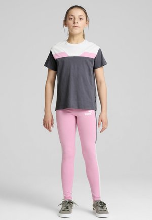 Camiseta gris y blanca con acentos rosas, combinada con leggins rosas que tienen una franja lateral. Zapatillas deportivas grises completan el atuendo.
