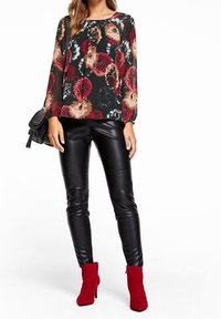 Blommig blus i svart, röd och krämfärgad med långa ärmar; tillsammans med glänsande svarta leggings och röda ankelstövlar. Svart axelv äska ingår.