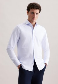 Witte blouse met knopen, gemaakt van een gladde stof, met een kraag, lange mouwen en een rechte zoom, gecombineerd met donkere broeken.
