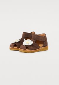 Sandales en suède marron avec un design à bout ouvert, ornées de marguerites blanches et d'une sangle autocollante pour la fermeture. Semelle texturée.