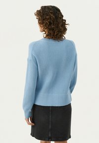 Pull en maille côtelée bleu clair avec un col rond, des épaules tombantes et un ourlet ajusté, porté sur une jupe en denim noire.
