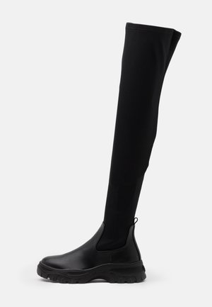 Botte noire montant au genou avec semelle épaisse et tige lisse, tige en tissu élastique et languette à l'arrière.