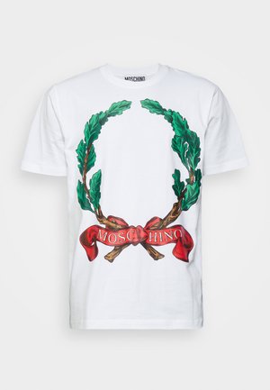 T-shirt bianco in cotone con una grande grafica di foglie di alloro verdi che circondano un nastro rosso con la scritta "MOSCHINO" stampata in bianco.