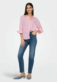 Blusa ricamata rosa chiaro con un motivo aperto, maniche arrotolate, abbinata a jeans blu a gamba dritta e décolleté azzurri con punta.