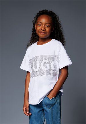 Hvit bomulls T-skjorte med et "HUGO" grafikk laget av små prikker, korte ermer og en avslappet passform, kombinert med blå jeans med en hjerteformet lomme.