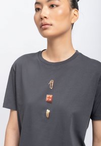 Grijze katoen T-shirt met een centrale grafische ontwerp featuring een paperclip, een rode blok en een beige tand in een verticale opstelling.