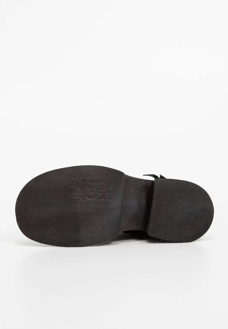 Schwarze Schuhsohle mit strukturiertem Finish. Verfügt über geprägtes Branding und einen glatten Bereich nahe der Ferse. Gebogene Form und flaches Design.
