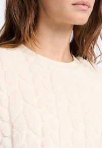 Kremowy sweter z polaru, z teksturowanym, wypukłym wzorem, okrągłym dekoltem i miękką, puszystą powierzchnią.