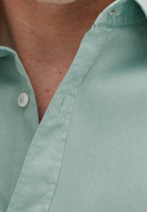 Hellgrünes Baumwollhemd mit Knopfleiste und Kragen. Der Stoff hat eine glatte Textur mit kontrastierenden Nähten und Knöpfen.